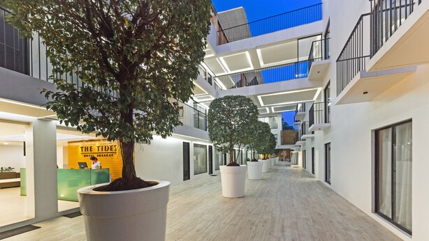 Un moderno vestíbulo de hotel con mostrador de recepción, grandes árboles en macetas y un amplio pasillo con techos altos y balcones.