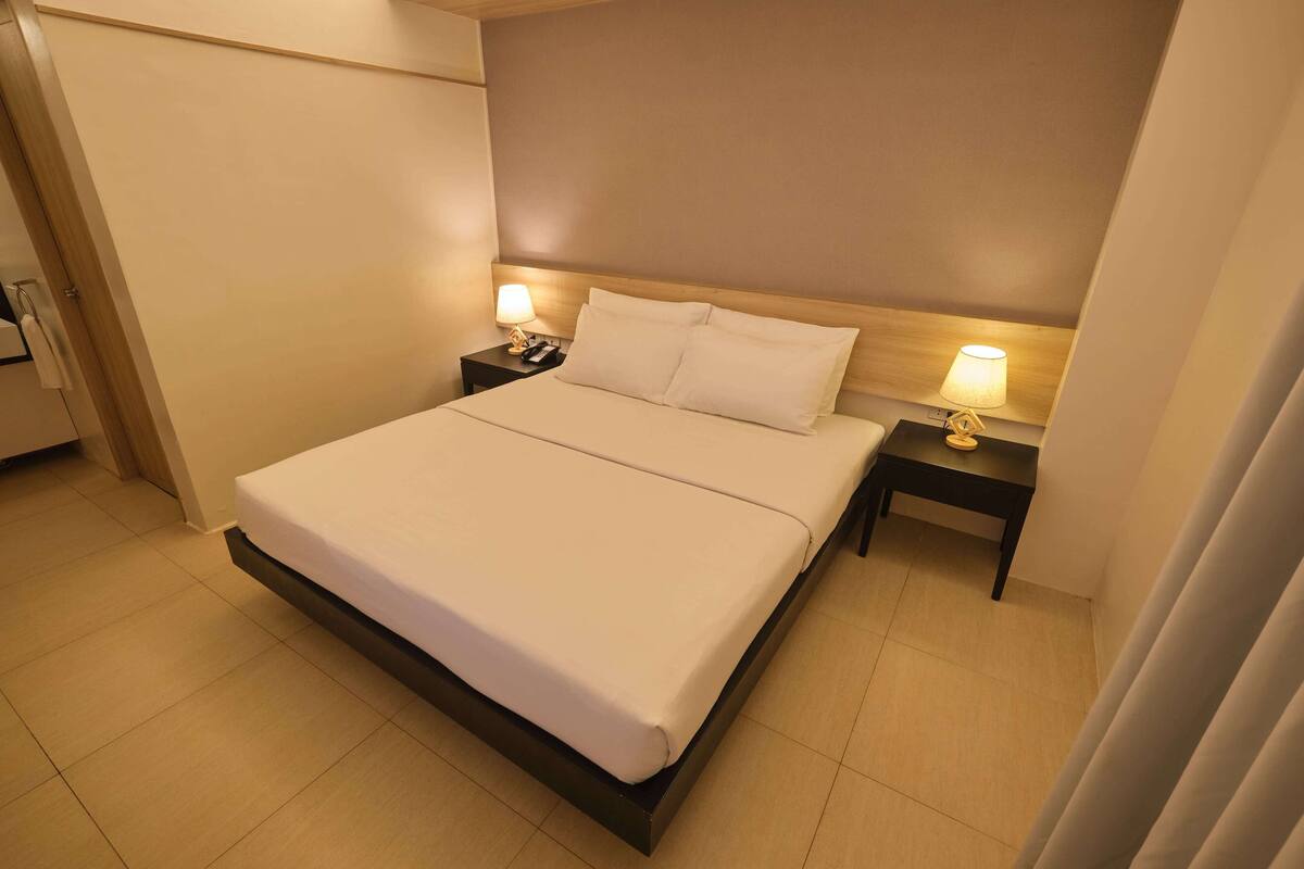 A neatly made bed with a wooden headboard, two bedside tables with lamps, and a tiled floor.