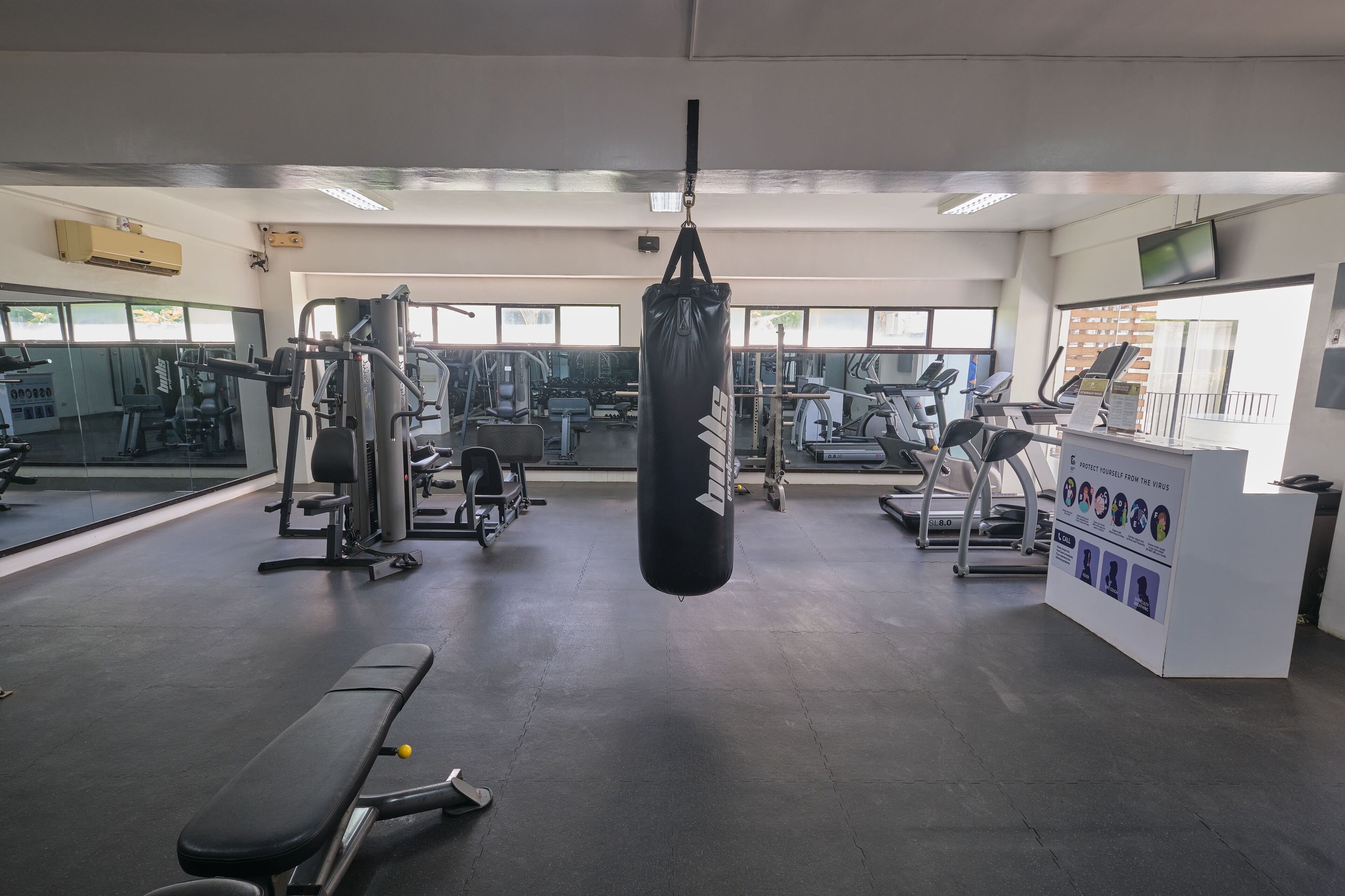 A gym with various exercise equipment, a punching bag, and a reception desk with informational posters.