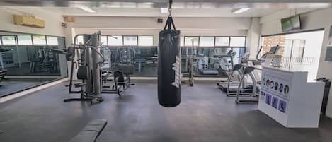 A gym with various exercise equipment, a punching bag, and a reception desk with informational posters.