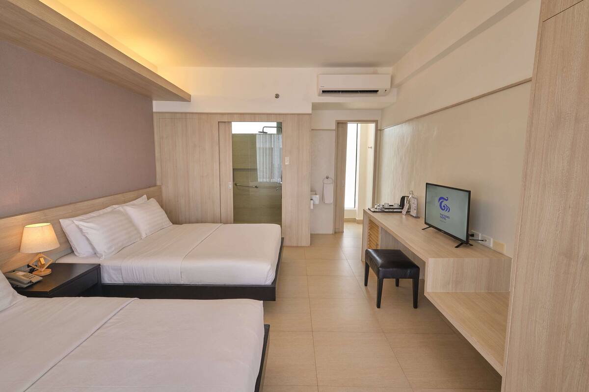 A hotel room with two beds, a desk with a TV, and a bathroom visible through an open door.