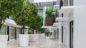 Un edificio moderno con un patio central que destaca por grandes árboles en macetas, suelo de mármol y fachada de vidrio.