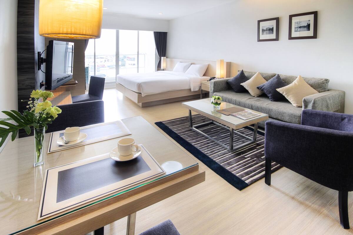 Una habitación de hotel moderna con cama, sofá y zona de comedor con mesa y sillas.