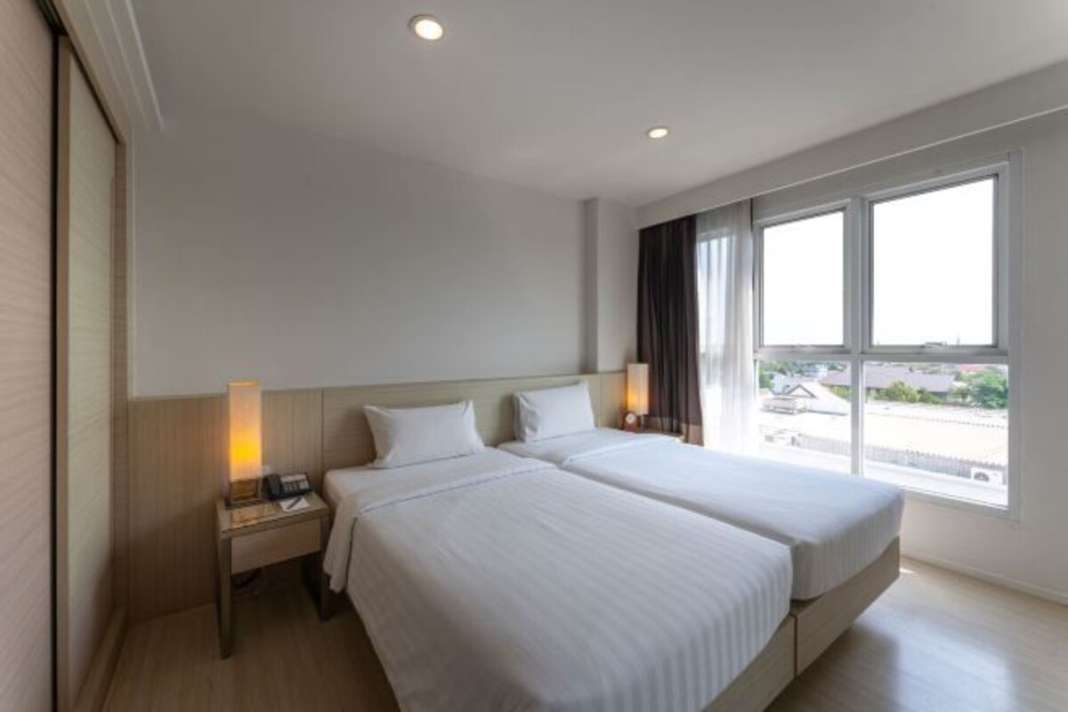 Una habitación de hotel con dos camas, una mesita de noche con lámpara y un ventanal con vistas al exterior.