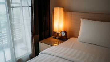 Une chambre d’hôtel avec un lit, une table de chevet avec une lampe et une vue par une fenêtre équipée de stores.