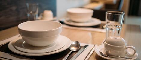 A dining table set with white plates, bowls, a cup, and cutlery.