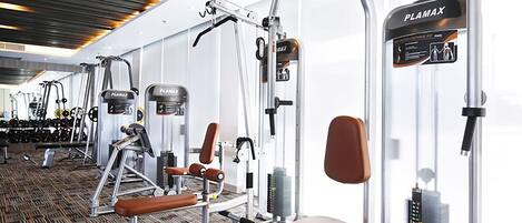 Un gimnasio con diversas máquinas de ejercicio, incluyendo una prensa de banca y una máquina de poleas, con un muro espejado y un suelo estampado.