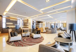 A spacious lobby with modern furniture, a central coffee table, and a large TV screen.