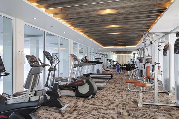 Un gimnasio moderno con diversas máquinas de cardio, equipo de levantamiento de pesas y una alfombra estampada.