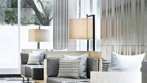 A modern living room with a sofa set, two floor lamps, and a view of the outdoors through large windows.