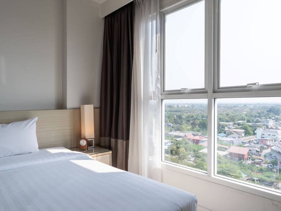 A hotel room with a large bed, a nightstand, a clock, and a window with a city view.