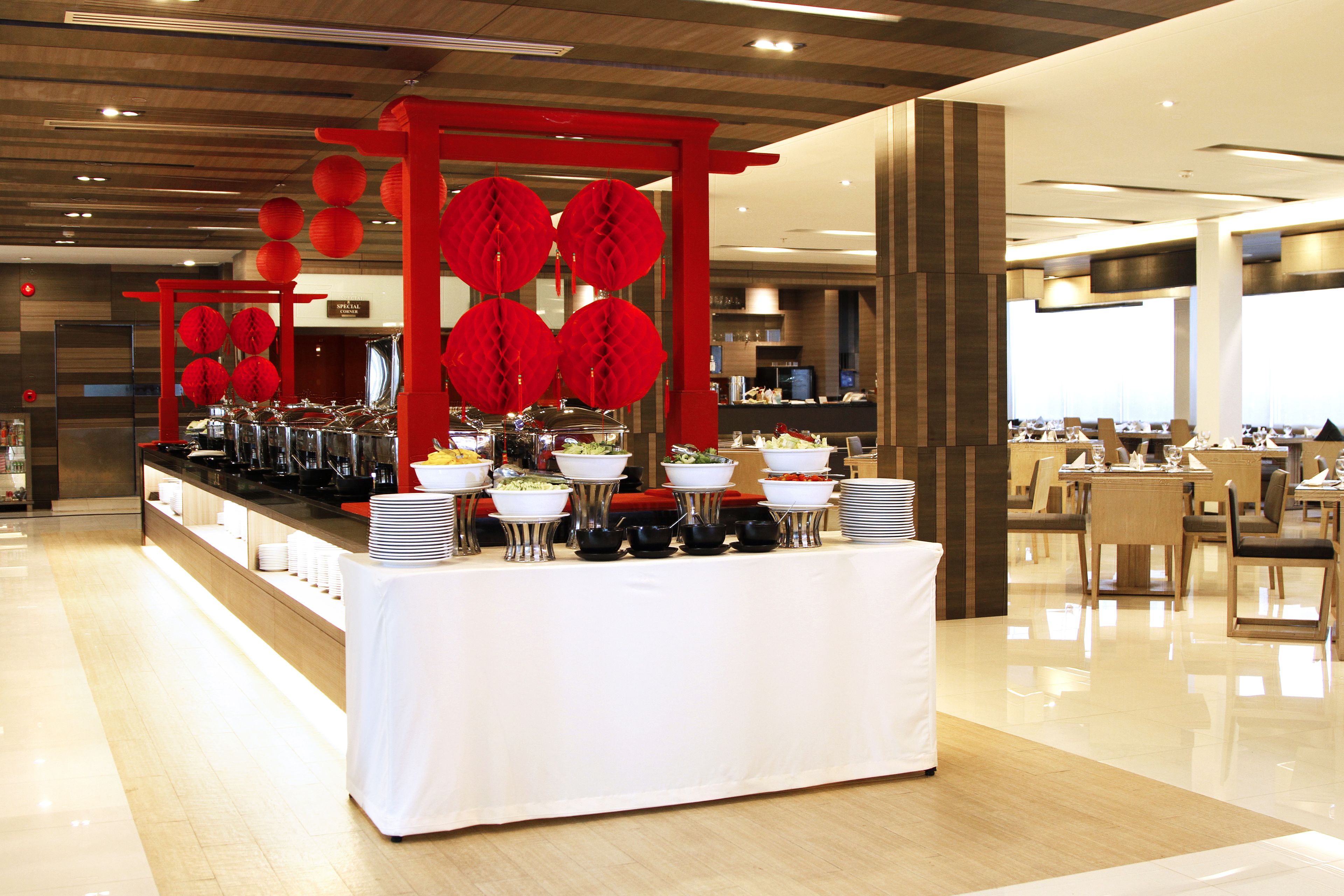 Montaje de bufé con diversas estaciones de comida, una estructura decorativa roja y un interior moderno y limpio.