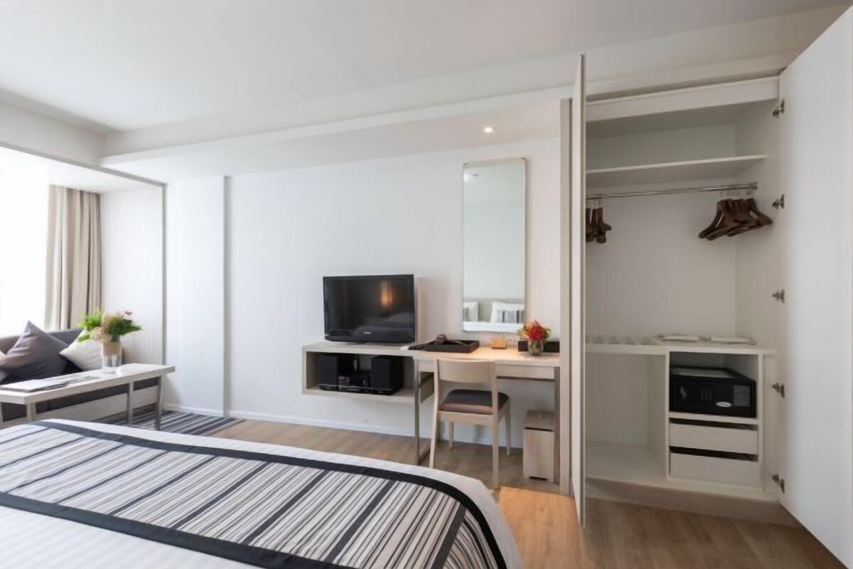 A modern hotel room with a bed, a desk, a television, a wardrobe, and a mirror.