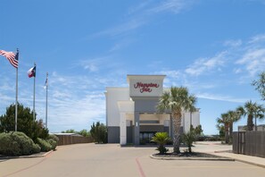 A Hampton Inn with a clear sky, American flags, and a parking lot. - Hampton Inn Pleasanton (Pleasanton)