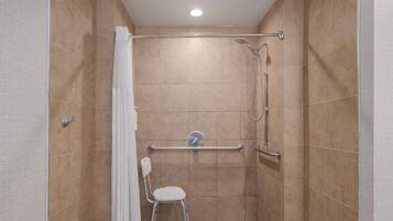A shower with a handheld showerhead, a handheld showerhead, a grab bar, and a white chair.