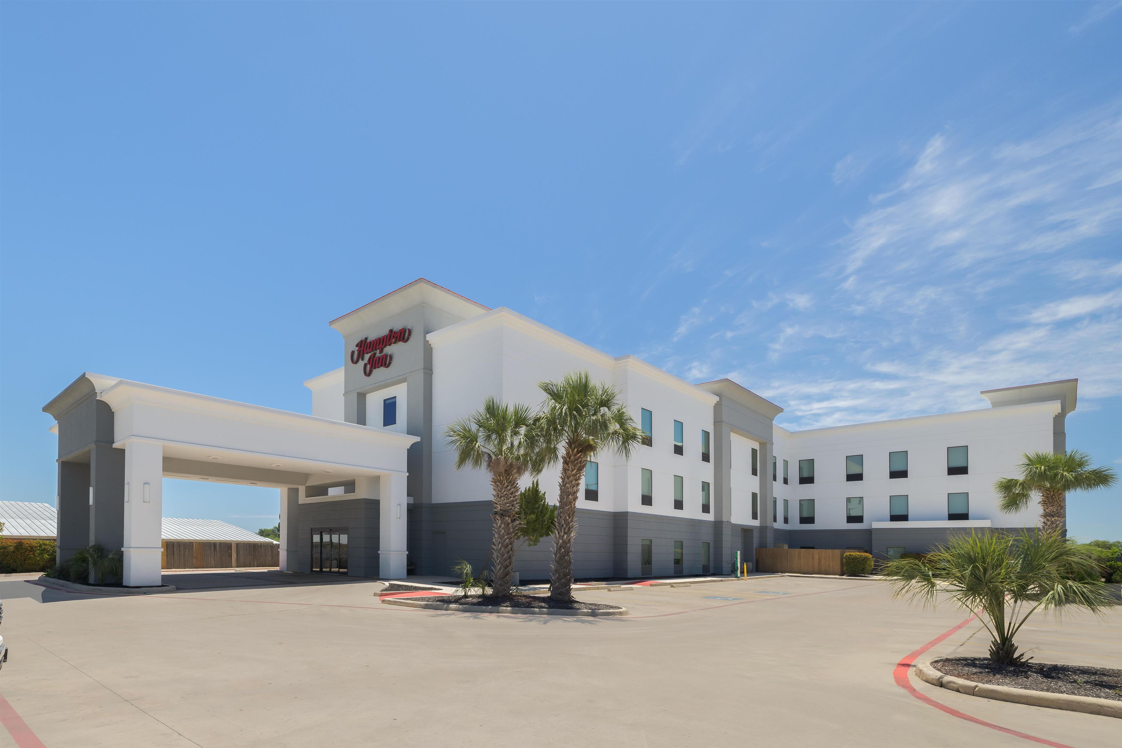 A modern hotel with a flat roof, a covered entrance, and palm trees in the courtyard.