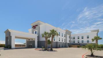A modern hotel with a flat roof, a covered entrance, and palm trees in the courtyard.