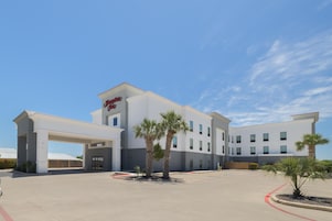 Un hotel moderno con techo plano, entrada cubierta y palmeras en el patio.