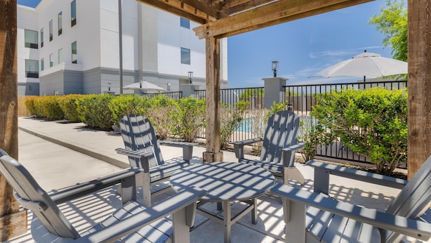 An outdoor seating area with Adirondack chairs and a table, a wooden pergola, a pool, and a modern building in the background.
