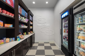 A hotel lobby with a checkered floor, a counter with snacks, a wall with hexagonal patterns, and a refrigerated display case. - Hampton Inn Pleasanton (Pleasanton)