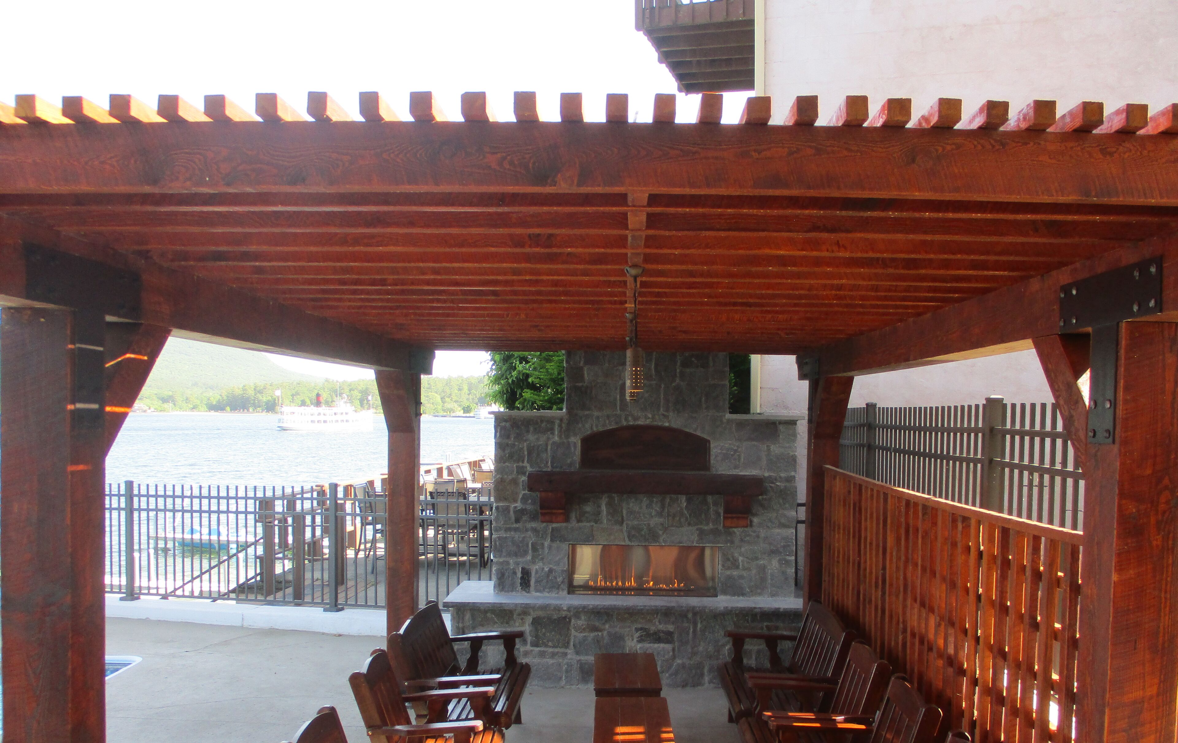 An outdoor patio with wooden furniture, a stone fireplace, and a view of the water.