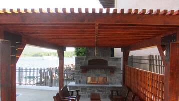 An outdoor patio with wooden furniture, a stone fireplace, and a view of the water.