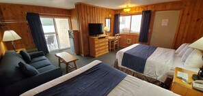 Quarto de hotel com cama, sofá, escrivaninha, televisão e janela com cortinas.