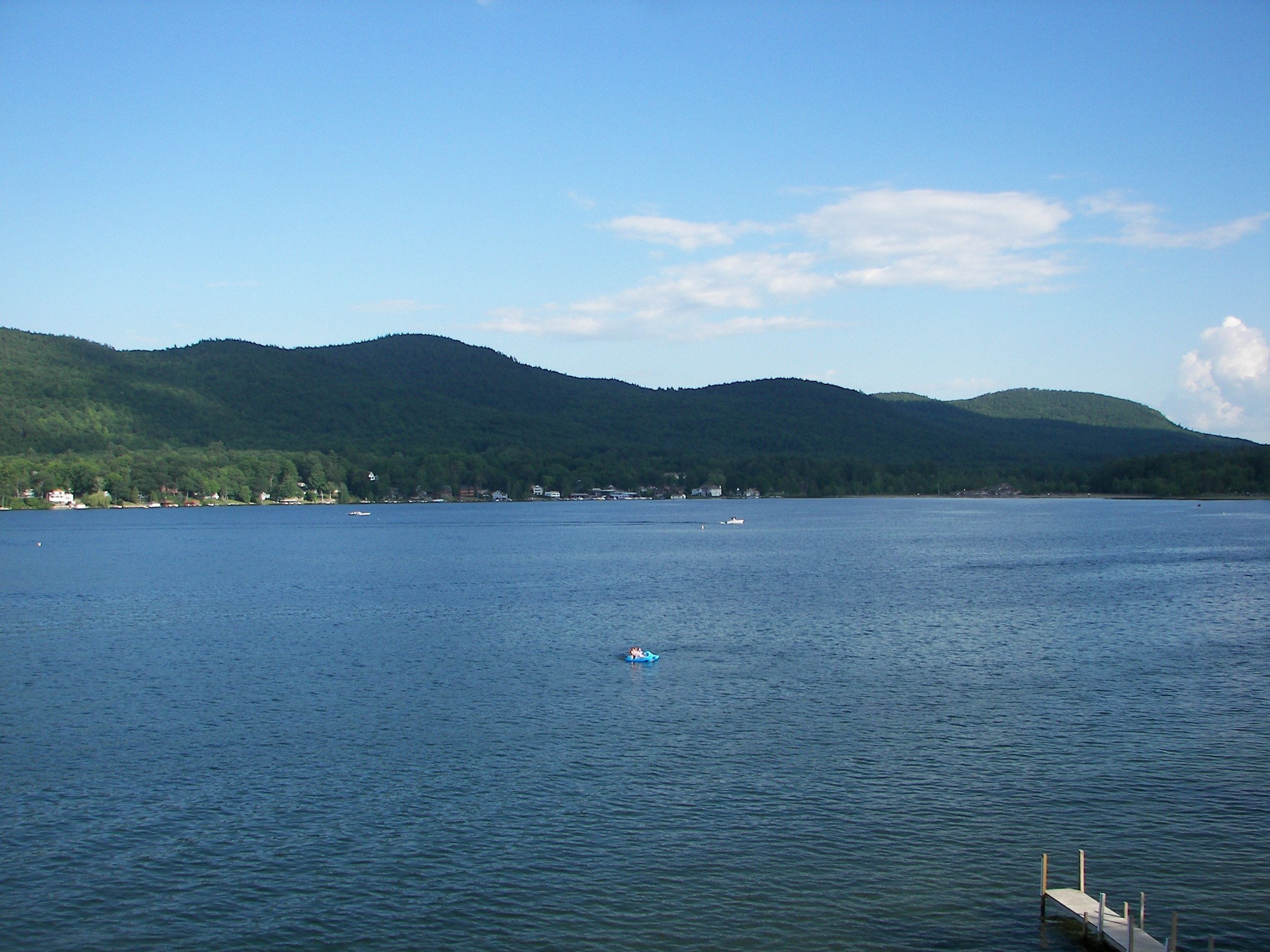 A calm lake with a dock extending into the water, surrounded by forested hills.