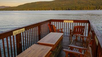 A wooden deck with a 'NO DIVING' sign, wooden benches, and chairs overlooking a lake with a forested hill in the background.