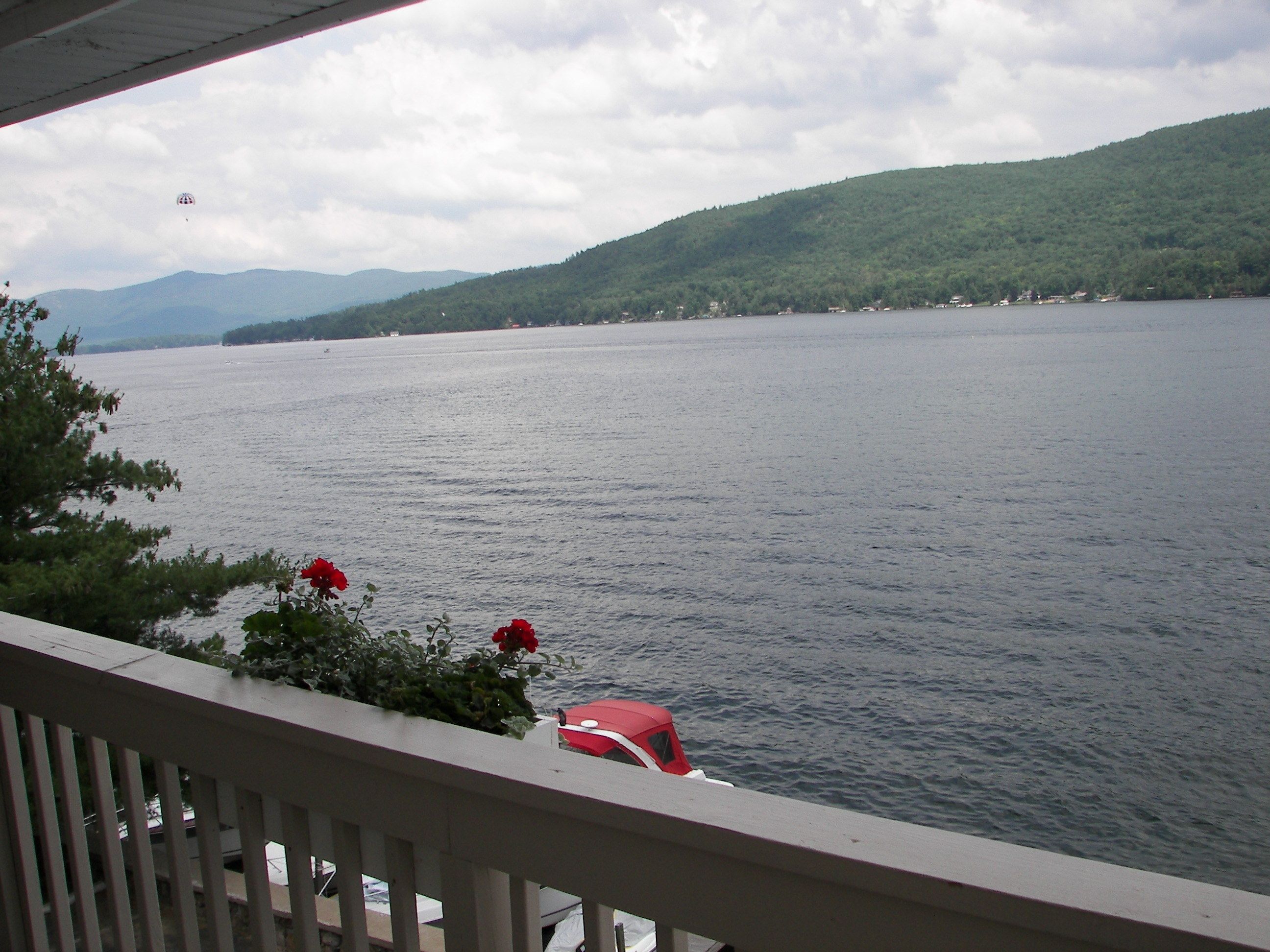 A view of a lake with a boat docked on the shore, surrounded by greenery and hills in the background.