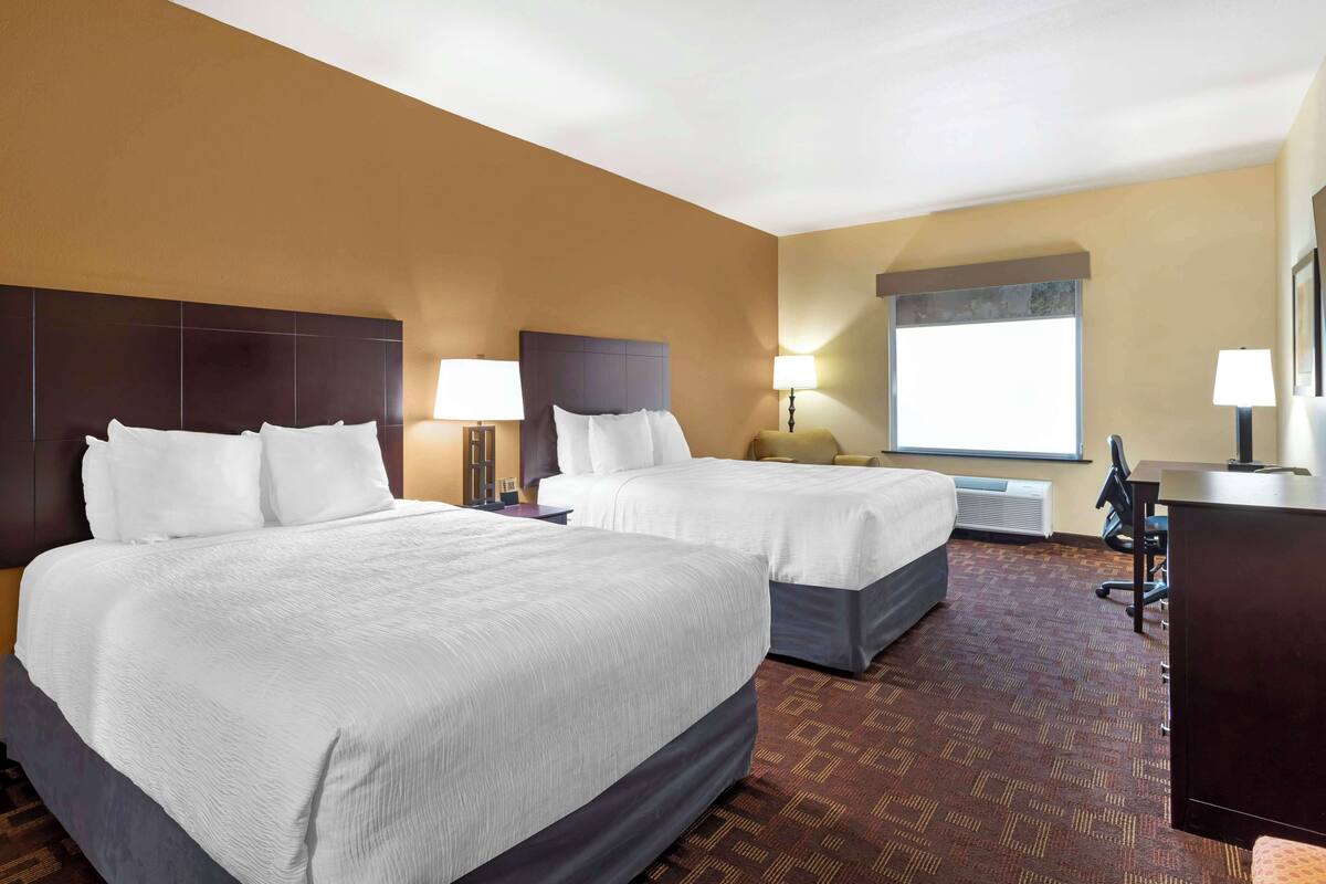 A hotel room with two beds, a desk, and a large window.