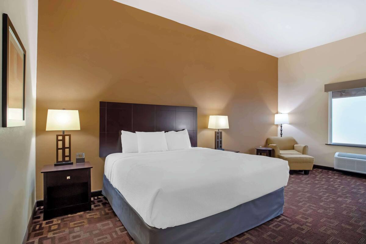 A hotel room with a large bed, two bedside tables with lamps, a chair, and a projector screen on the wall.
