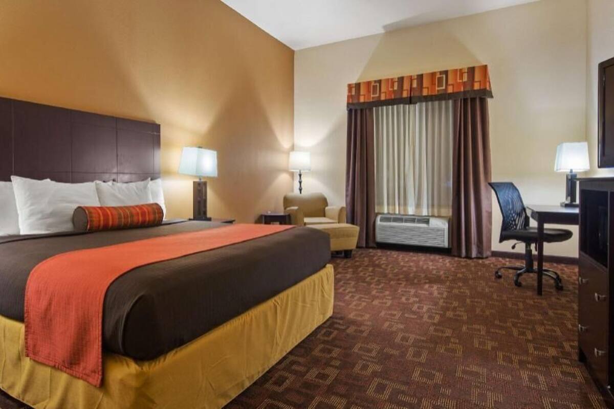 A hotel room with a large bed, a desk, a chair, an air conditioning unit, and a television.