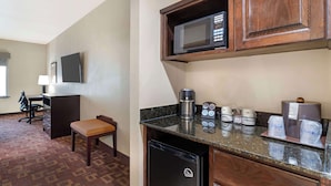 Une chambre d’hôtel compacte comprenant un coin cuisine, un bureau avec une chaise et un petit espace salon.