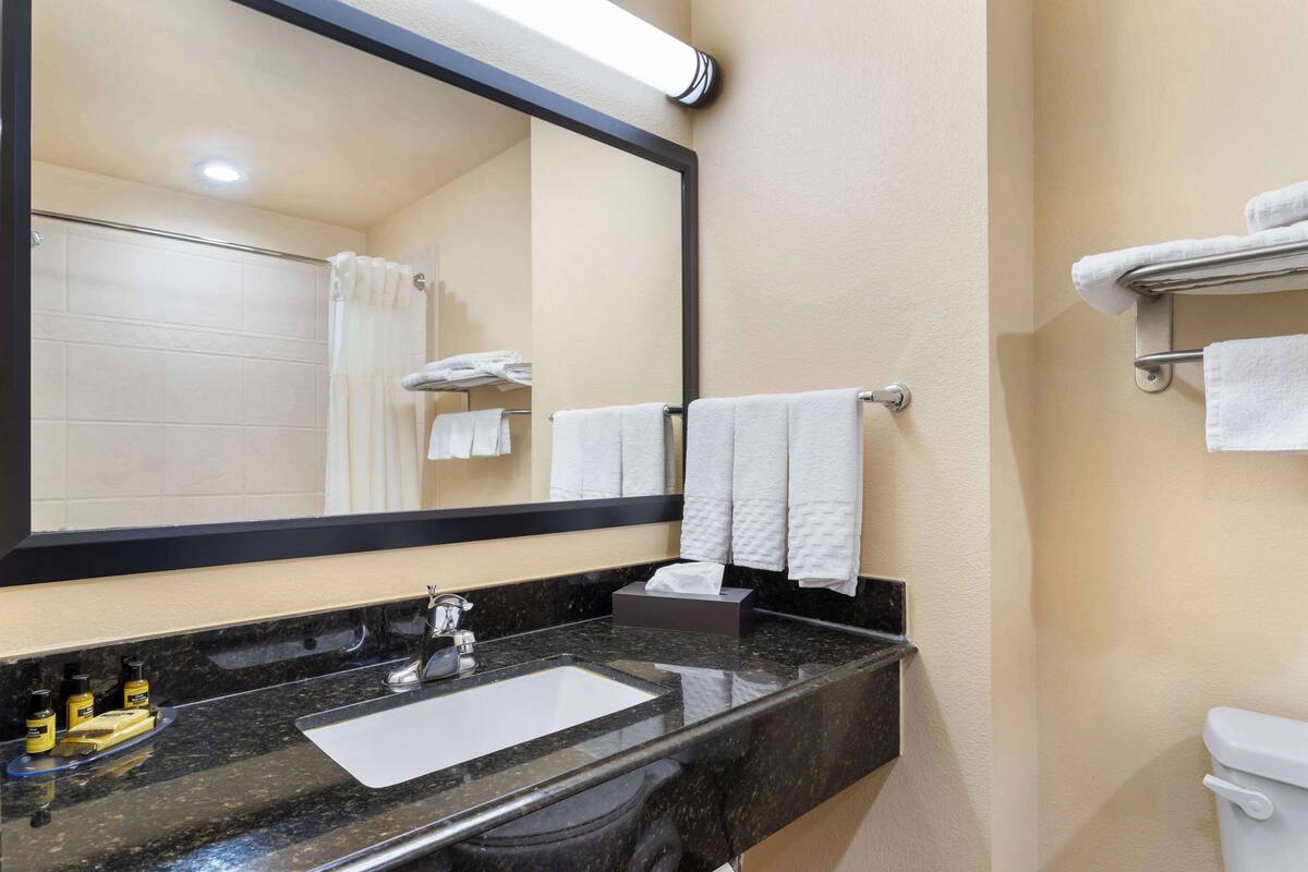 A bathroom with a black marble sink, a large mirror, a toilet, and a towel rack with multiple white towels.