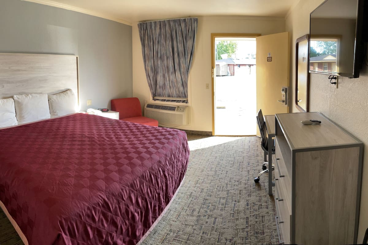 A bedroom with a large bed, a desk, a chair, a dresser, and a television.