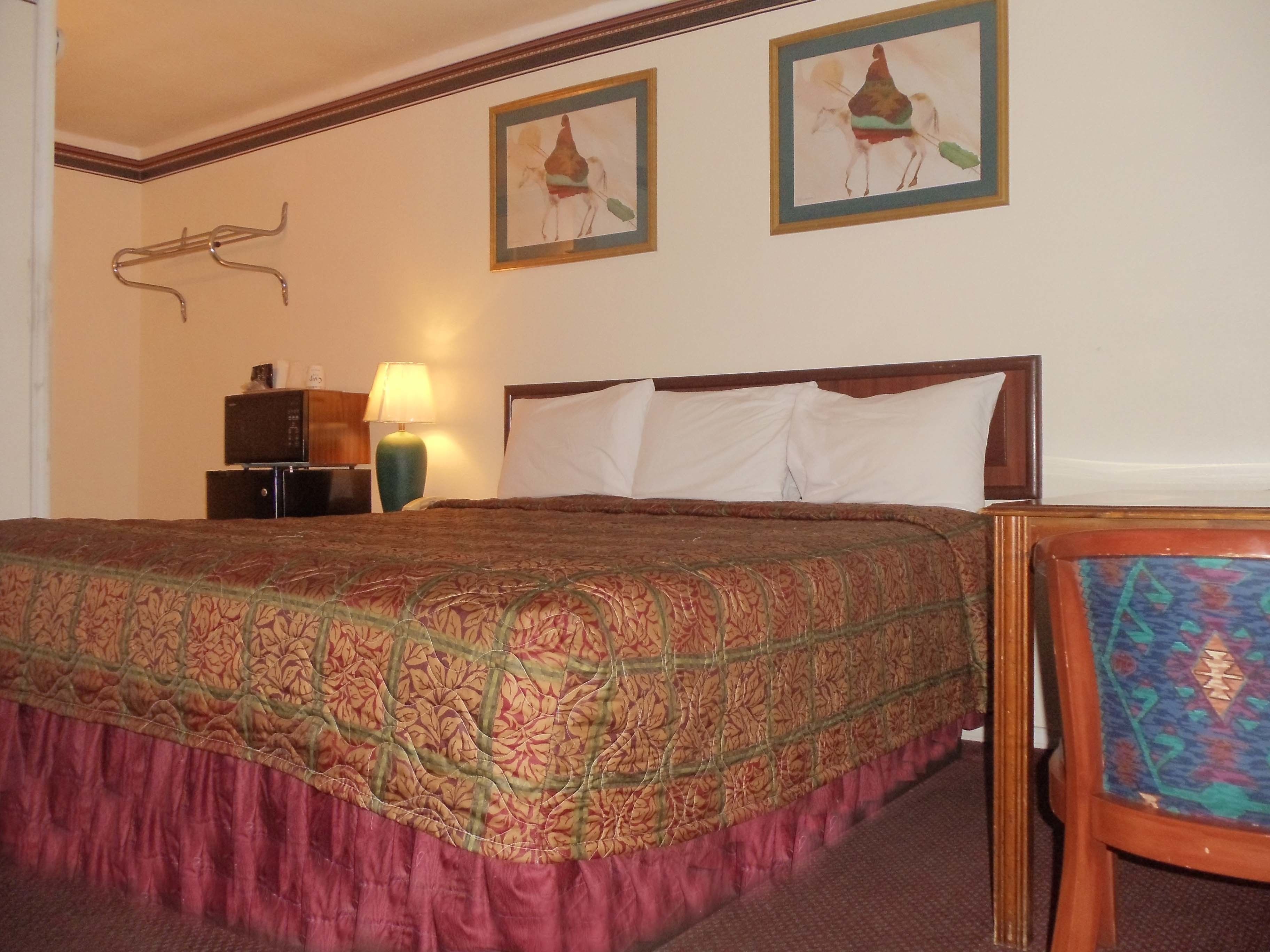 Habitación de hotel con una cama grande, una mesita de noche con lámpara y dos cuadros en la pared.