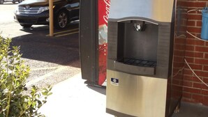A stainless steel outdoor kitchen with a Coca-Cola branded refrigerator, a water dispenser, and a sink. - Antlers Budget Inn (Antlers)