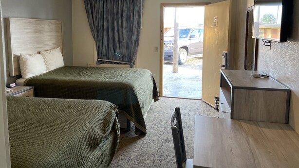 A hotel room with two beds, a desk, a chair, a television, and a view of the outside. - Antlers Budget Inn (Antlers)