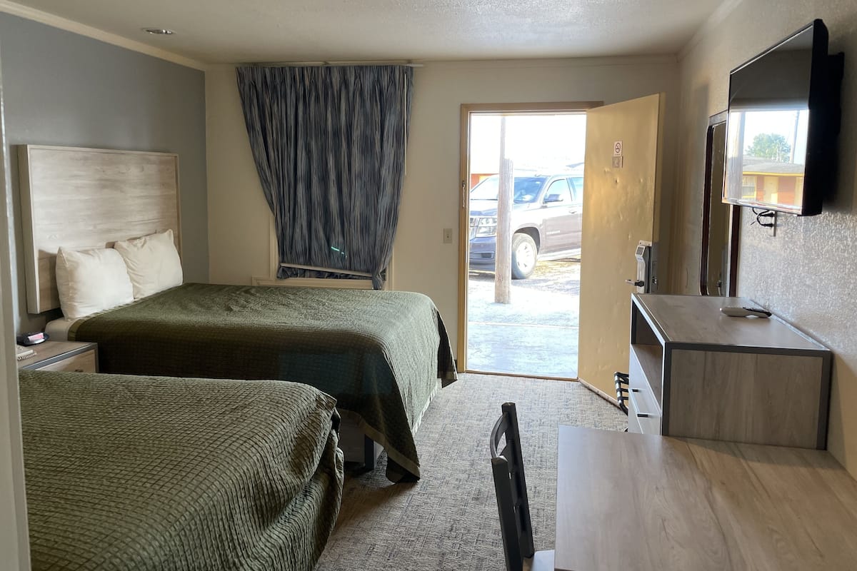 A hotel room with two beds, a desk, a chair, a television, and a view of the outside.