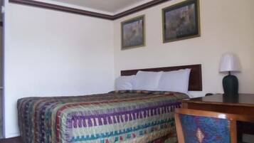 A hotel room with a neatly made bed, a wooden nightstand with a lamp, and two framed pictures on the wall.