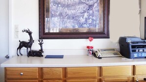 A kitchen counter with a framed wildlife painting, a printer, a mug, and a small deer figurine. - Antlers Budget Inn (Antlers)