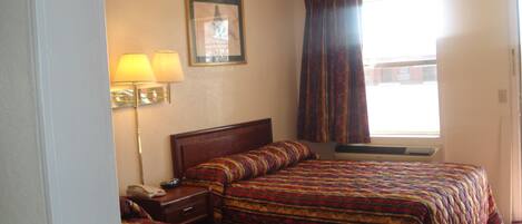Habitación de hotel con dos camas, una mesita de noche, una lámpara y un ventanal con cortinas.