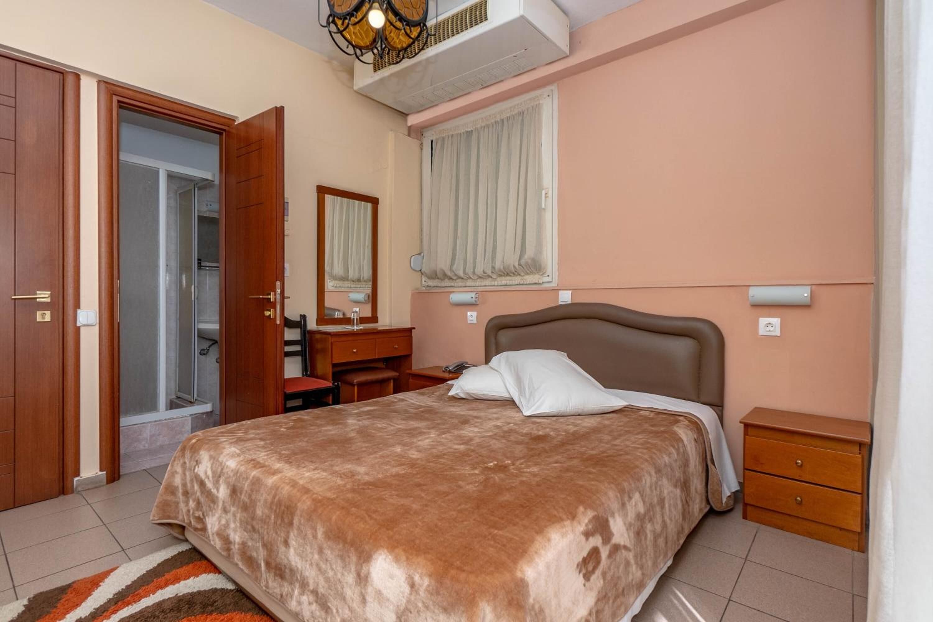 A bedroom with a large bed, a desk, a chair, a wardrobe, and a window with curtains.