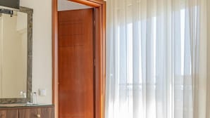 Una habitación de hotel con puerta de madera, baño con espejo y cama con toalla doblada.