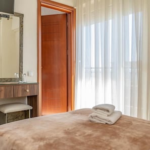 A hotel room with a wooden door, a bathroom with a mirror, and a bed with a folded towel. - Hotel Alkyon (Alexandroupoli)