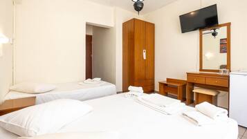 Habitación de hotel con dos camas, un armario de madera, un escritorio con silla, un televisor montado en la pared y una lámpara en el techo.