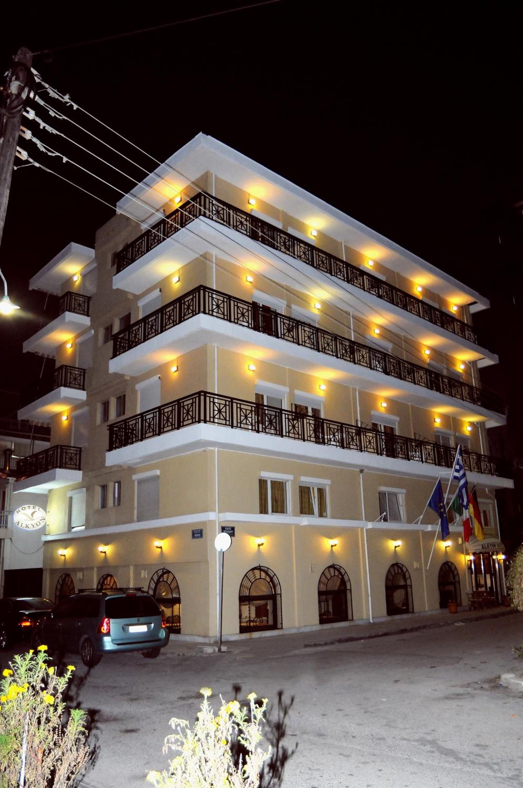 A multi-story hotel with balconies, a parking area, and flags.