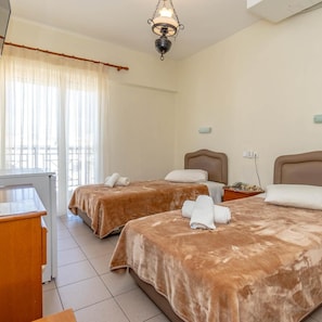A hotel room with two beds, a desk, a chair, a lamp, and a window with curtains. - Hotel Alkyon (Alexandroupoli)
