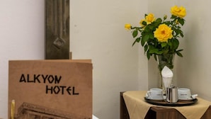 Letrero de hotel con ilustración de un edificio, un jarrón con flores amarillas y una mesa con tetera y tazas.